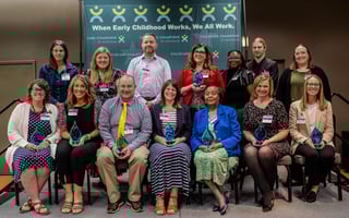 Group photo of the 2025 Childcare Champions of Michigan award winners on stage, holding glass trophies before a banner reading “When Early Childhood Works, We All Work.”