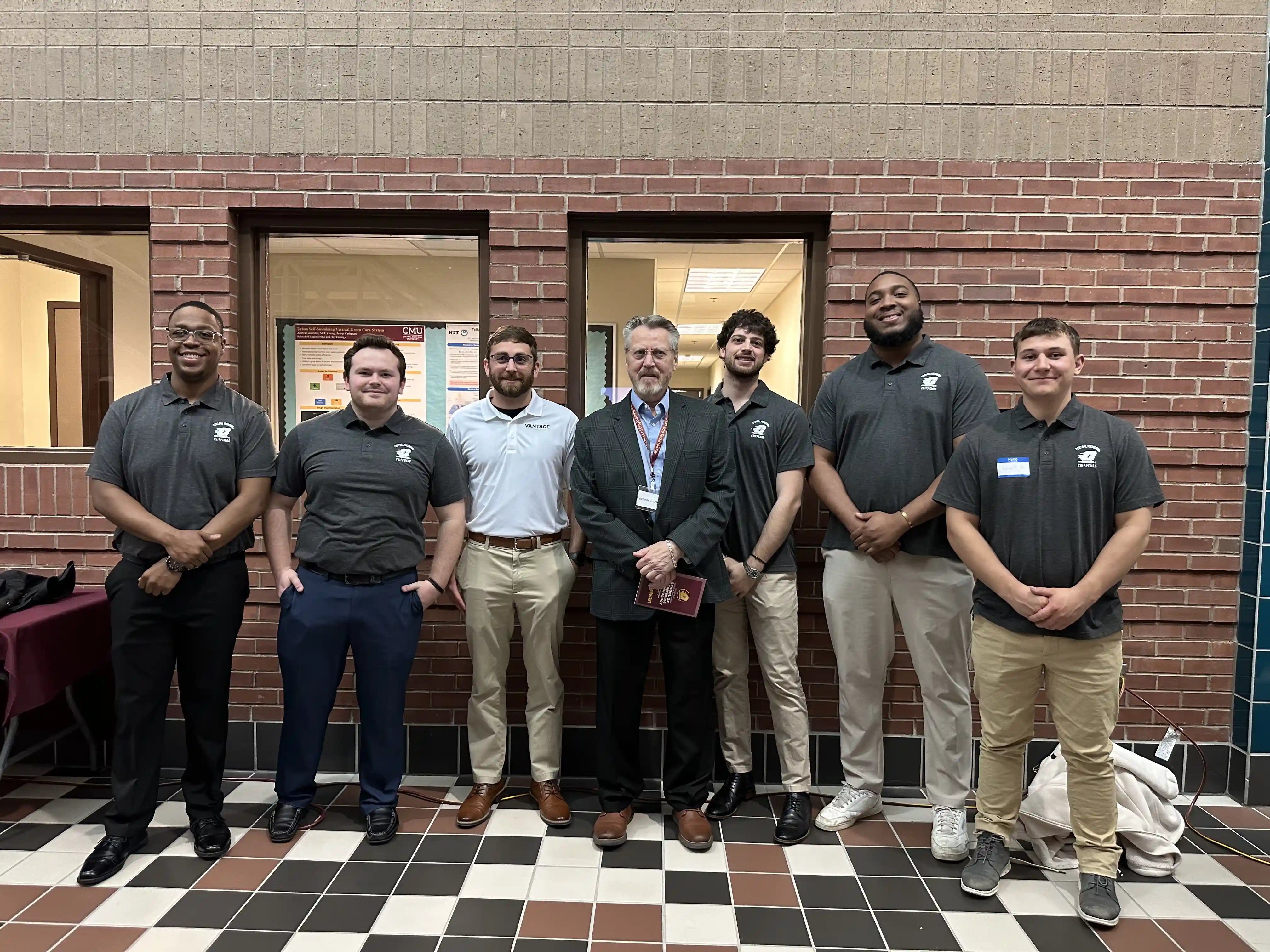 George Aultman and John Tatton stand with CMU engineering students at the Senior Design Expo in front of their project display.